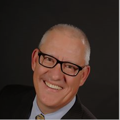 A man with glasses and a suit smiling.